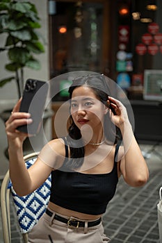 A gorgeous Asian woman is taking selfies with her smartphone while relaxing in a cafe in the city