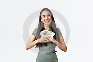 Gorgeous asian woman winning prize, holding money and smiling, thinking what to buy, earn cash for her startup, small