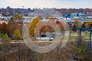 A gorgeous autumn landscape in the city with a circular park surrounded by autumn colored trees with tall light posts