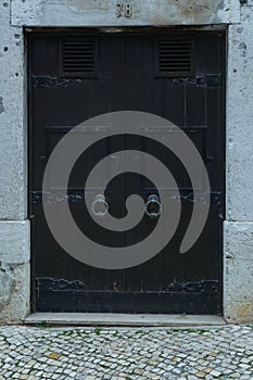 Gorgeous big old ancient black wooden door of stone building with knocker decorated with forgings carving. Architecture.