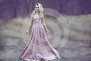 Gorgeous blond lady with luxuriant hairstyle in long brocade dress walking along the narrow path in the woods photo