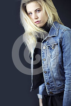 A gorgeous blond woman with messy hair, black turtleneck and jean jacket.