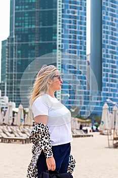 A gorgeous blonde woman in Dubai, UAE is enjoying the beach scenery amidst contemporary architecal designs