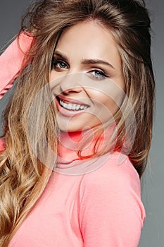 Gorgeous blonde woman in pink sweater with wavy volumed hair.