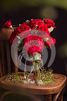 Gorgeous bouquet of red roses in a jug on an old wooden chair on a black background with bokeh