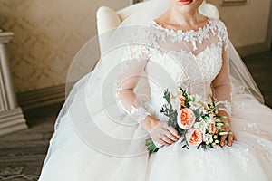 Gorgeous bouquet of white and orange flowers in the hands of the charming woman in a white dress. Bride sit on the chair