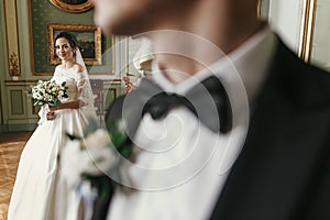 Gorgeous bride in amazing dress with bouquet and stylish groom posing in luxury room in hotel. rich wedding couple. romantic