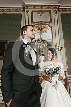 Gorgeous bride in amazing dress with bouquet and stylish groom posing in luxury room in hotel. rich wedding couple. romantic