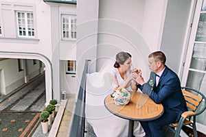Gorgeous bride and elegant groom sit at the table on balcony. Newlyweds honeymoon concept