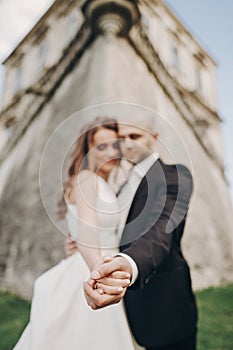 Gorgeous bride and groom embracing, holding hands closeup near old castle in park. Romantic moment. Stylish wedding couple gently