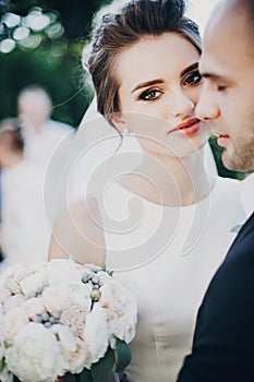 Gorgeous bride and groom gently hugging in sunset light. Beautiful stylish wedding couple embracing in summer park. Sensual