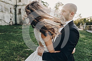 Gorgeous bride and groom having fun and dancing in evening sunlight near old castle in park. Stylish wedding couple gently