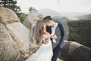 Gorgeous bride, groom kissing and hugging near the cliffs with stunning views