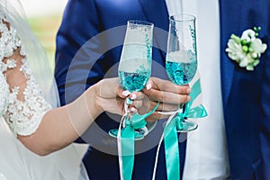 Gorgeous bride and groom toasting with champagne, wedding morning. hands holding stylish glasses of blue wine