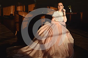 Gorgeous bride in luxurious puffy wedding dress with veiling skirt sitting in the armchair photo