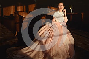 Gorgeous bride in luxurious puffy wedding dress with veiling skirt sitting in the armchair