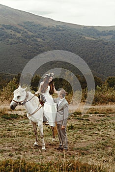 Gorgeous bride riding a white horse and stylish groom, boho wed