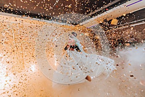 Gorgeous bride and stylish groom dancing under golden confetti at wedding reception.