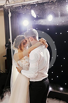 Gorgeous bride and stylish groom gently dancing at wedding reception. Happy wedding couple performing first dance in restaurant.