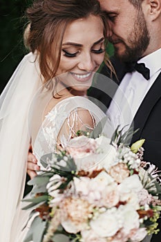 Gorgeous bride and stylish groom gently hugging and smiling on b photo