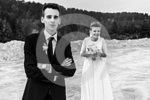 Gorgeous bride and stylish groom holding hands and looking at sandy beach lake, black and white photo, luxury wedding