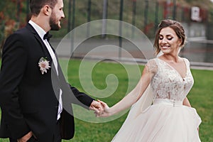 Gorgeous bride and stylish groom holding hands and walking at wa