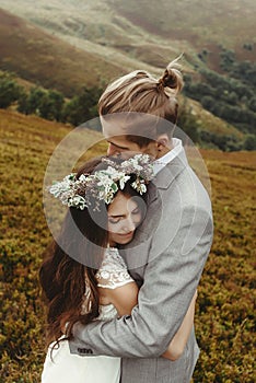 Gorgeous bride and stylish groom hugging at sunny landscape, bo