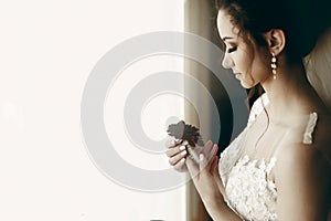 Gorgeous bride in vintage lace white wedding dress holding red flower, portait of beautiful woman posing near a window, wedding