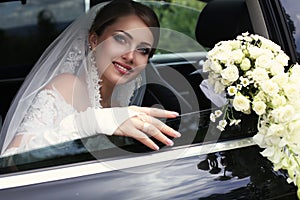 Gorgeous bride in wedding dress with bouquet of flowers posing in car
