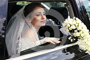 Gorgeous bride in wedding dress with bouquet of flowers posing in car
