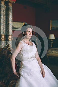 Gorgeous bride in wedding dress in luxury interior with diamond jewelry posing at home and waiting for groom