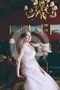 Gorgeous bride in wedding dress in luxury interior with diamond jewelry posing at home and waiting for groom