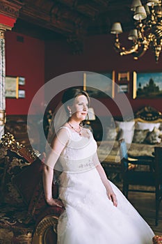 Gorgeous bride in wedding dress in luxury interior with diamond jewelry posing at home and waiting for groom