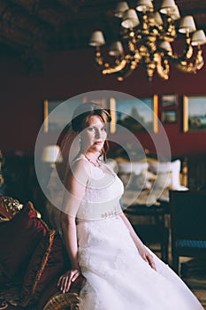 Gorgeous bride in wedding dress in luxury interior with diamond jewelry posing at home and waiting for groom