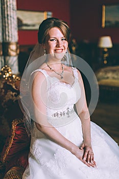 Gorgeous bride in wedding dress in luxury interior with diamond jewelry posing at home and waiting for groom