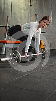 Gorgeous brunette female with long braids doing squats using barbell. Side view of srtong concentrated fitnesswoman with perfect