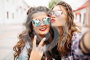 Gorgeous brunette girlfriends with hairstyle, mirrored sunglasses and red lips making selfie with duck face.