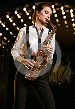 Gorgeous brunette model woman in fashionable formal suit with saxophone