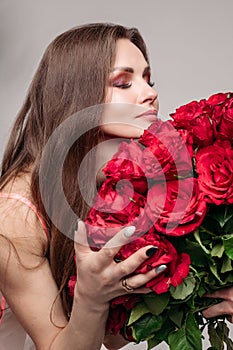 Gorgeous brunette woman in night gown smelling red roses.