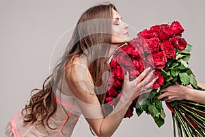 Gorgeous brunette woman in night gown smelling red roses.