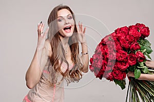 Gorgeous brunette woman in night gown smelling red roses.