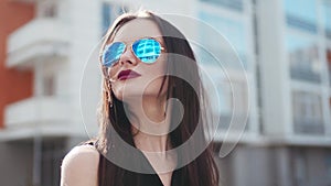 Gorgeous brunette woman with passionate red lips, and nose piercing looks to the camera and puts on the sunglasses