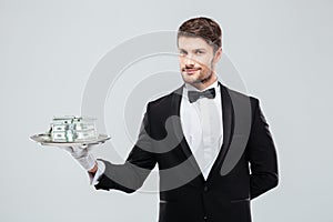 Gorgeous butler in tuxedo standing and holding tray with money