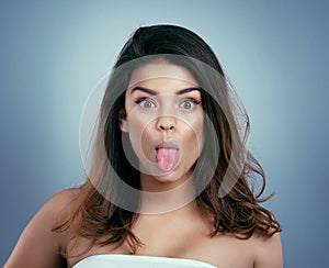 Gorgeous can be silly too. Studio shot of a beautiful young woman sticking out her tongue against a blue background.