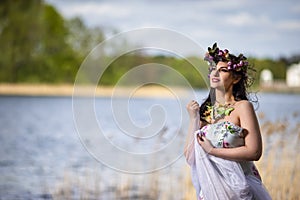 Gorgeous Caucasian Brunette Woman in Decorated Dress and Flowery Chaplet with Butterflies. Posing Against Nature Background