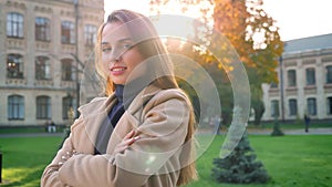 Gorgeous caucasian woman is looking at camera while standing chill and smiling happily in sunlights, urban background