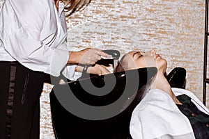 Gorgeous cute young woman enjoying head massage while professional hairdresser applying shampoo her hair. Close up of hairdresser