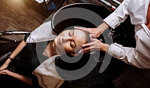 Gorgeous cute young woman enjoying head massage while professional hairdresser applying shampoo her hair. Close up of hairdresser