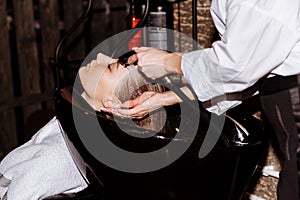 Gorgeous cute young woman enjoying head massage while professional hairdresser applying shampoo her hair. Close up of hairdresser