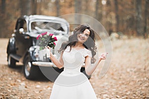 Gorgeous elegant bride posing near stylish retro black car Luxury wedding in vintage style. Portrait